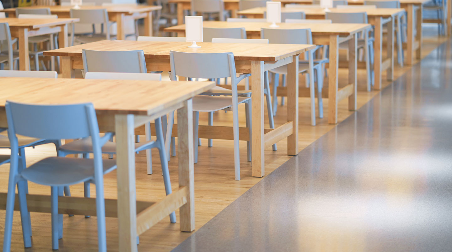Main tenant un devis posé sur une table en inox, arrière-plan de cantine scolaire.